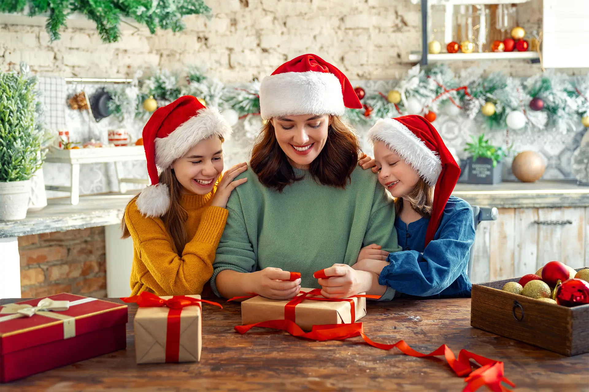 Mother and two daughters wrapping gifts wearing Santa hats.