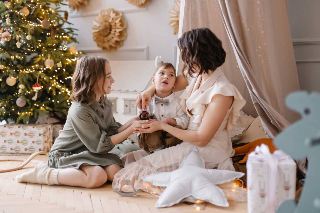 Adult with 2 children sitting near a Christmas tree.