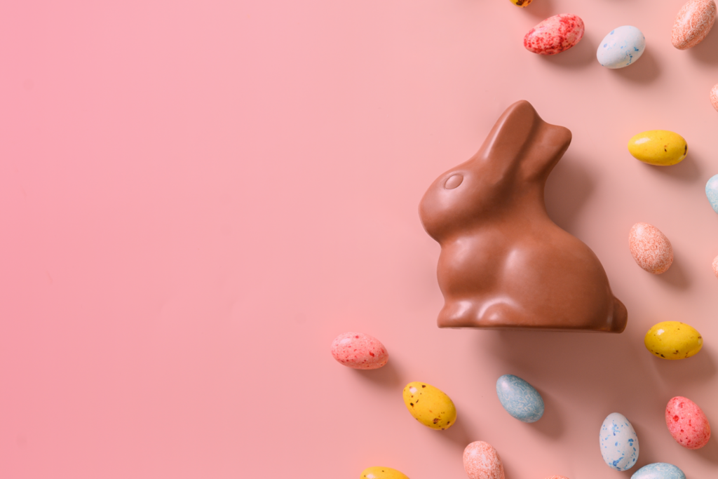 Chocolate Easter Bunny on pink background with colourful eggs scattered around.