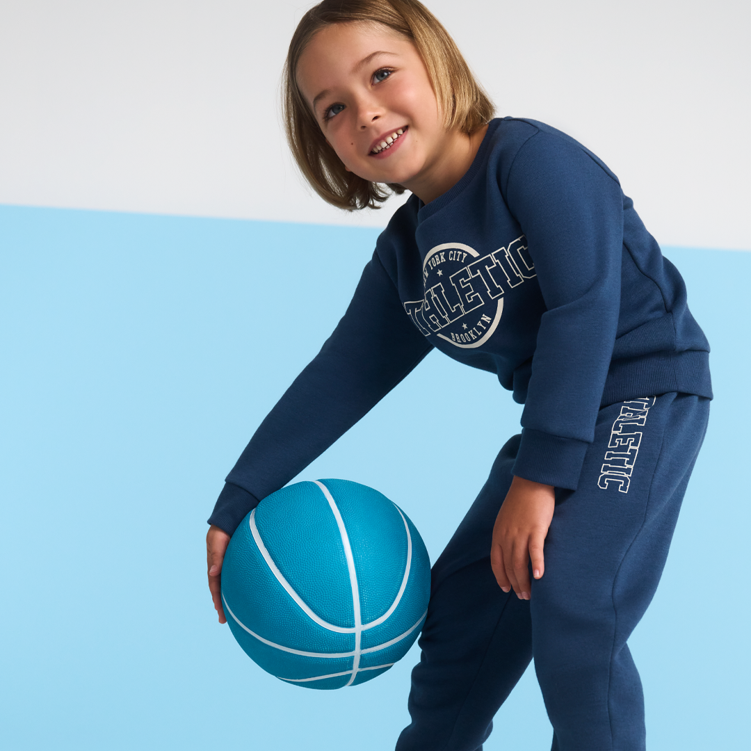 young child dressed in blue tracksuit and holding a blue basketball