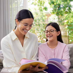 Mother and daughter wear glasses, reading a book and smiling