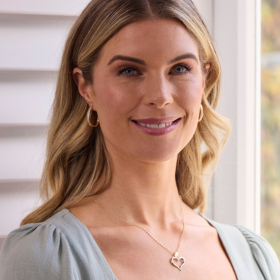 Woman wearing pale green dress and gold heart shaped necklace and gold hoop earrings
