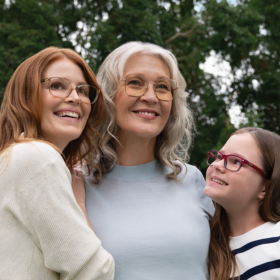Grandmother, daughter and granddaughter hugging and smiling wearing glasses