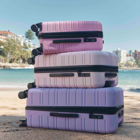 Three suitcases stacked on top of each other, the suitcases are purple, pink and light pink.