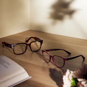 A pair of glasses sitting on a wooden table, next to an open book.